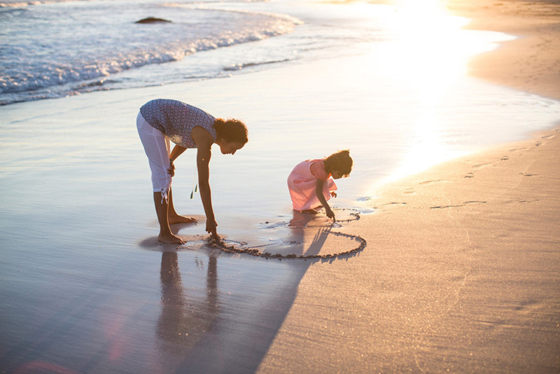 Mother and daughter drawing a heart and having fun together on the beach at sunset