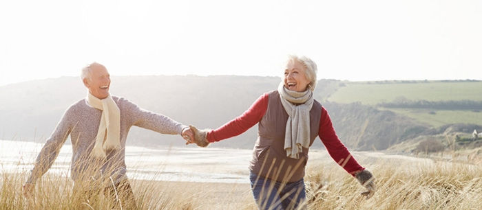 Senior Couple Walking Through Sand Dunes On Winter Beach Having Fun